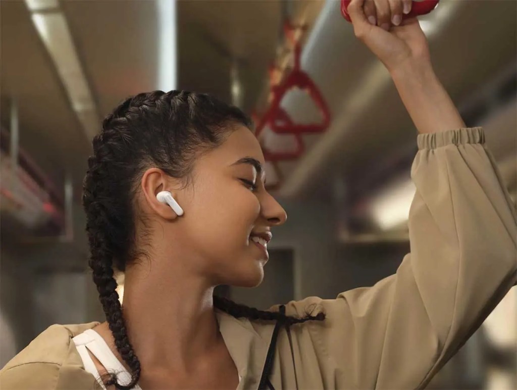 Una persona sonriente usando los HUAWEI FreeBuds 7i mientras se sostiene de un pasamanos en un transporte público.