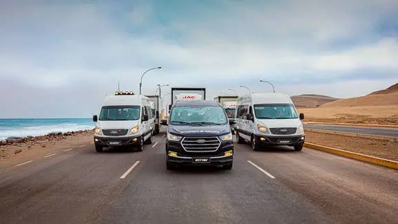 Imagen de varios modelos de vehículos comerciales de JAC en una carretera cerca del mar, incluyendo camionetas y vans.