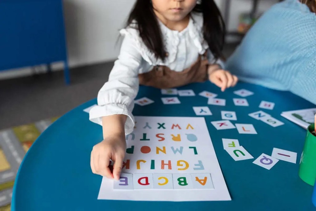 Una niña jugando con letras de colores sobre una mesa, mientras organiza las letras en una hoja de papel.