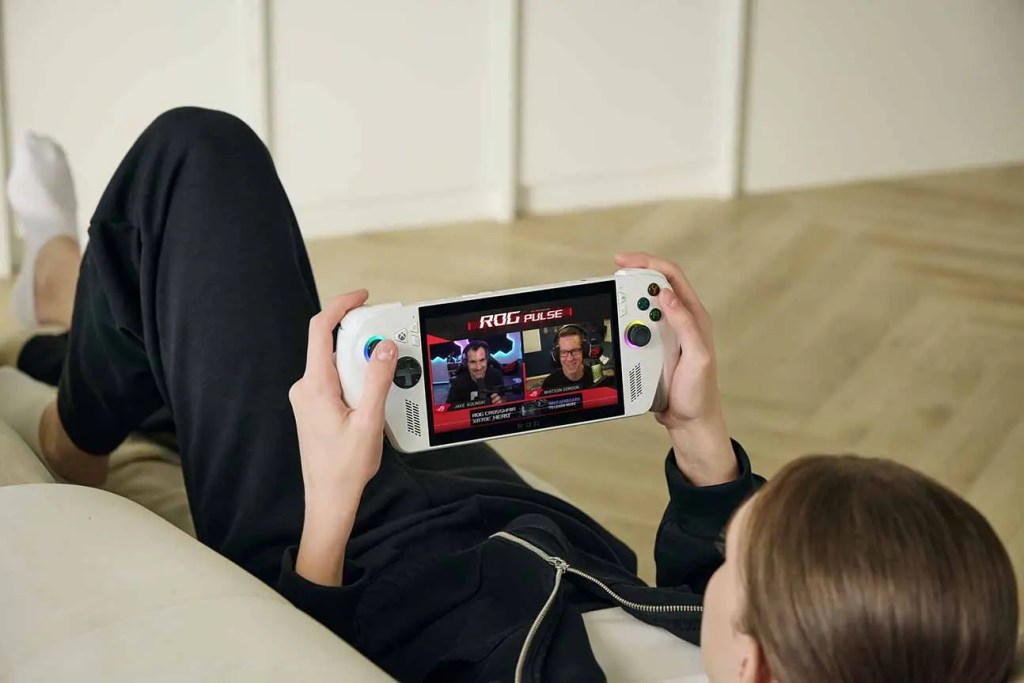 Una persona relaxada, acostada en un sofá, sostiene una consola portátil ROG Xbox Ally mientras juega y observa la pantalla que muestra contenido de videojuegos.