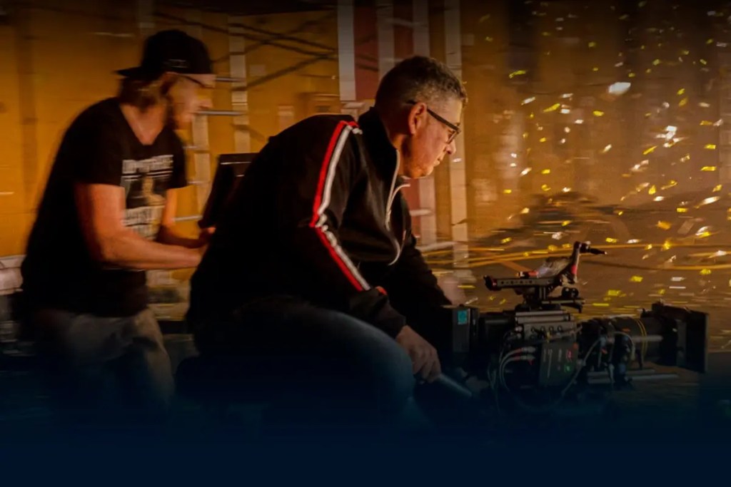 Un operador de cámara enfocado en una grabación, mientras otro asistente se prepara en un entorno de producción audiovisual.