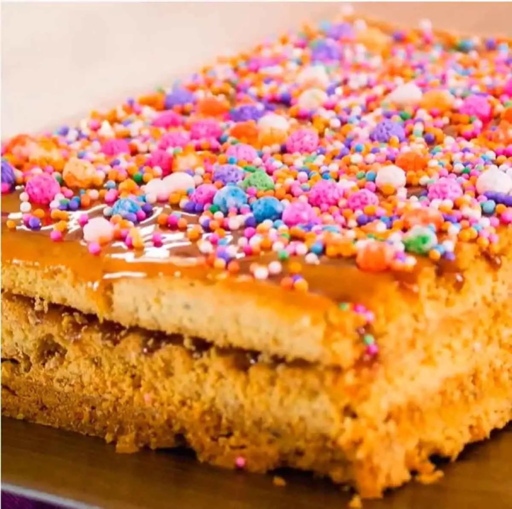 Un turrón de Doña Pepa decorado con coloridos confites y miel, típico postre peruano, presentado en una mesa.