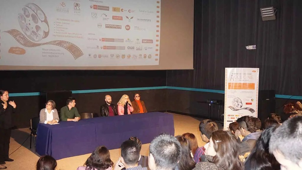 Panel de discusión en un evento de cine accesible, con participantes en una mesa y una audiencia atenta. Hay pantallas y un cartel del Festival de Cine Accesible AcceCine en el fondo.