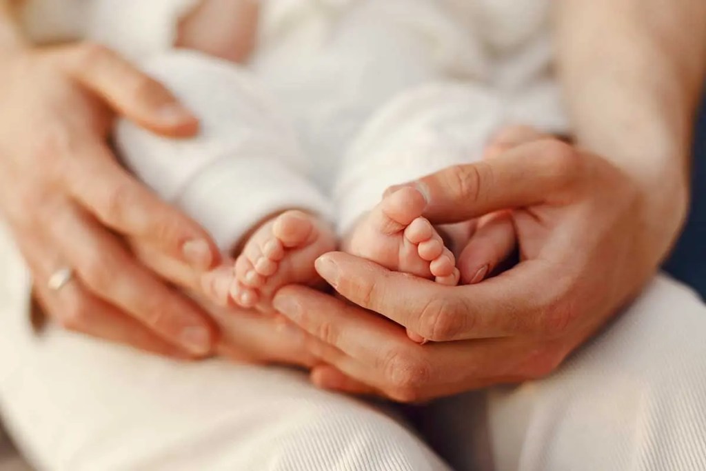 Manos de un adulto sosteniendo los pies de un bebé, simbolizando la atención y el cuidado de los recién nacidos.