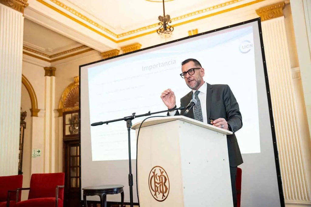 Un orador presenta información sobre el Tratado de Alta Mar durante un evento en Lima, con una pantalla de fondo que destaca su importancia.