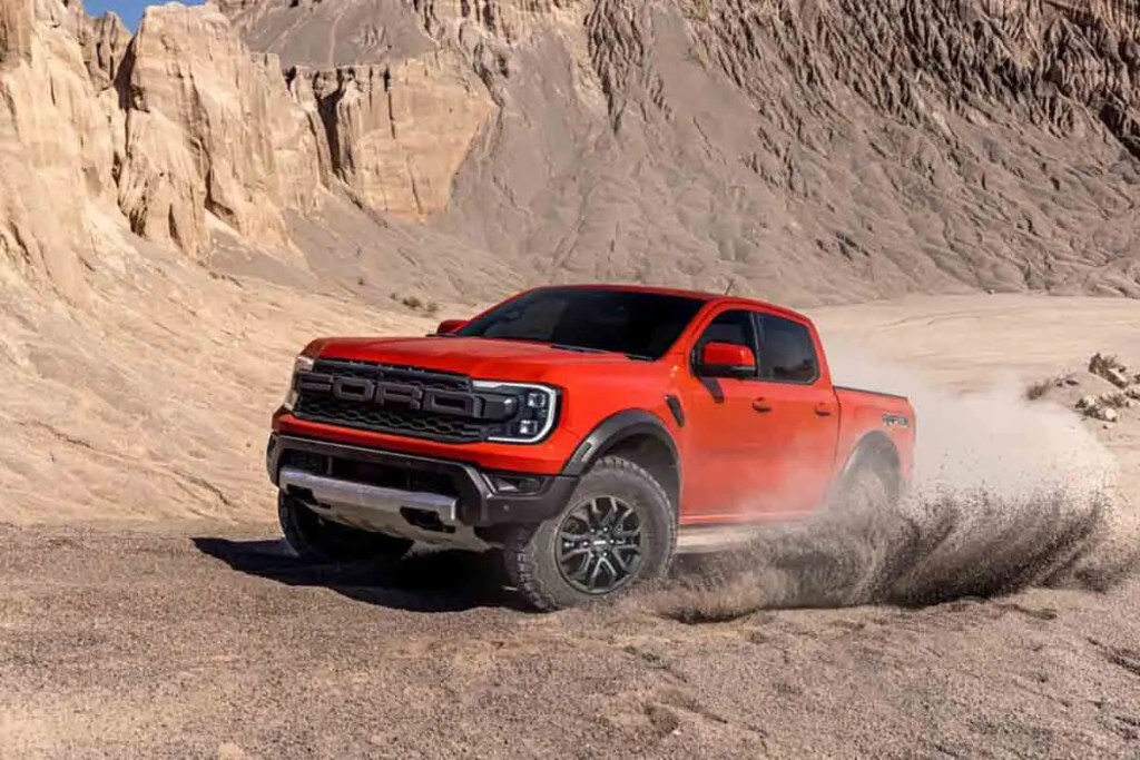 Pick-up Ford Raptor de color rojo avanzando sobre terreno arenoso con montañas en el fondo.