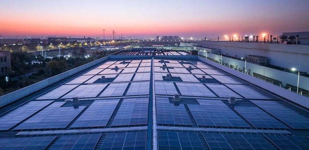 Vista de paneles solares en el techo de un edificio, con un atardecer colorido de fondo, destacando la transición hacia energías limpias.
