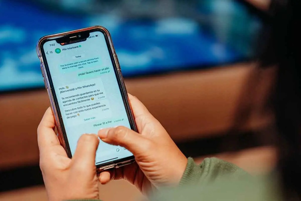 Persona usando un teléfono celular para interactuar con la aplicación de WhatsApp de Interbank, mostrando el asistente Plin WhatsApp en la pantalla.