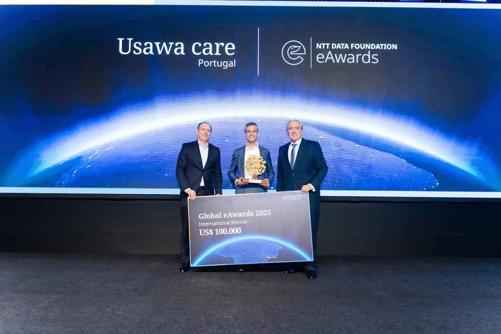 Tres personas en un escenario sosteniendo un trofeo y un cartel que indica 'Global eAwards 2025 International Winner US$ 100,000' con una presentación visual detrás que muestra un enfoque de la Tierra.