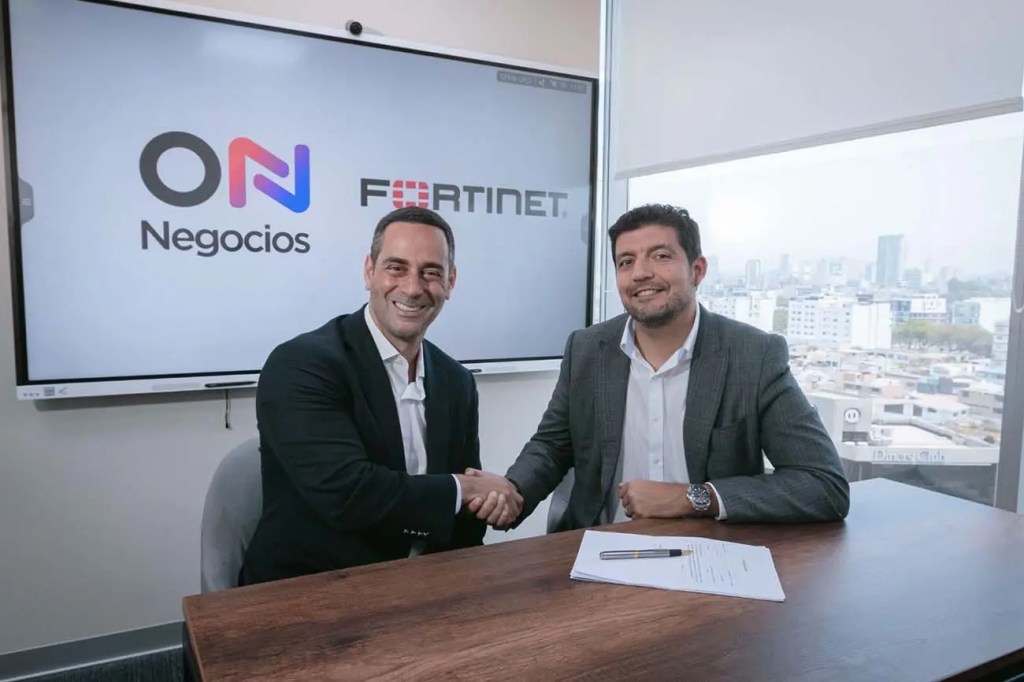 Dos hombres de negocios se estrechan la mano en una sala de reuniones, con los logotipos de ON Negocios y Fortinet visibles en una pantalla detrás de ellos.