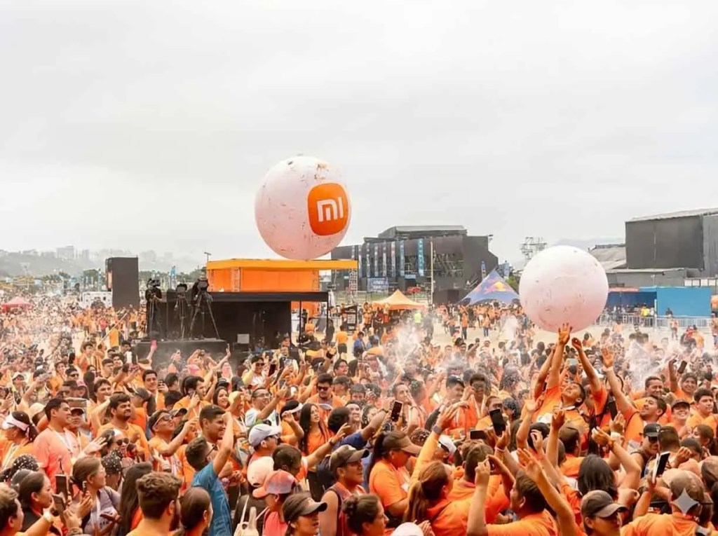 Gran multitud de participantes vestidos de naranja en el evento Xiaomi Pop Run 2025, con globos grandes de la marca en el aire y un ambiente festivo en la Costa Verde.