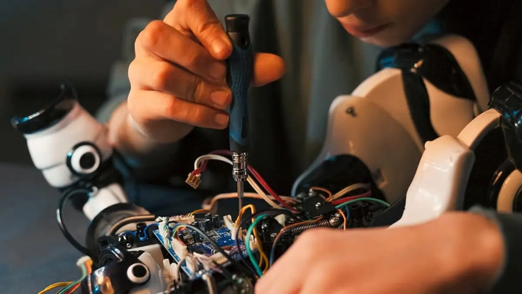 Una persona ajustando componentes electrónicos en un robot, mostrando elementos de cables y una pequeña herramienta.
