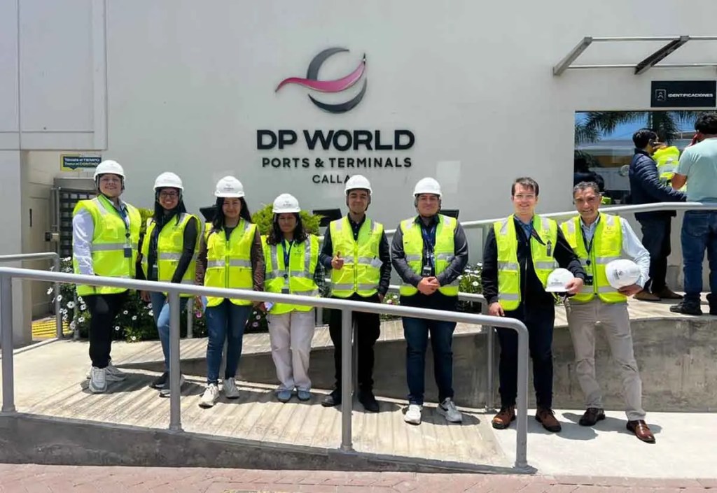 Grupo de profesionales en el Puerto de Chancay, vistiendo chalecos de seguridad y cascos, posando frente al edificio de DP World.