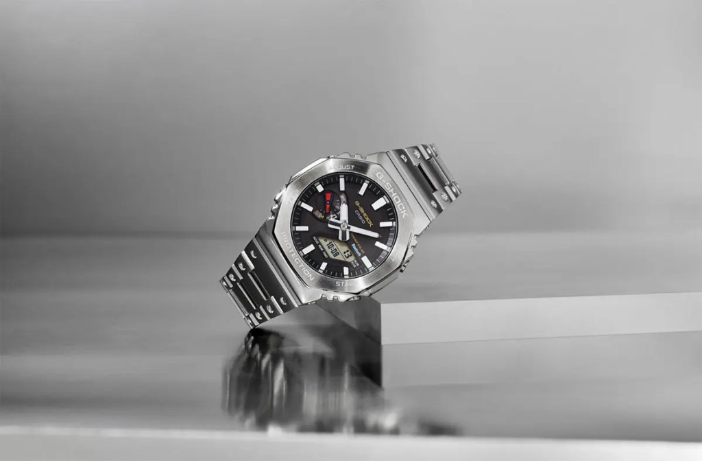 Reloj G-SHOCK de la colección Full Metal W/ Origen Colors, presentado en un fondo minimalista, mostrando su diseño metálico contemporáneo con un dial negro y detalles en colores clásicos.