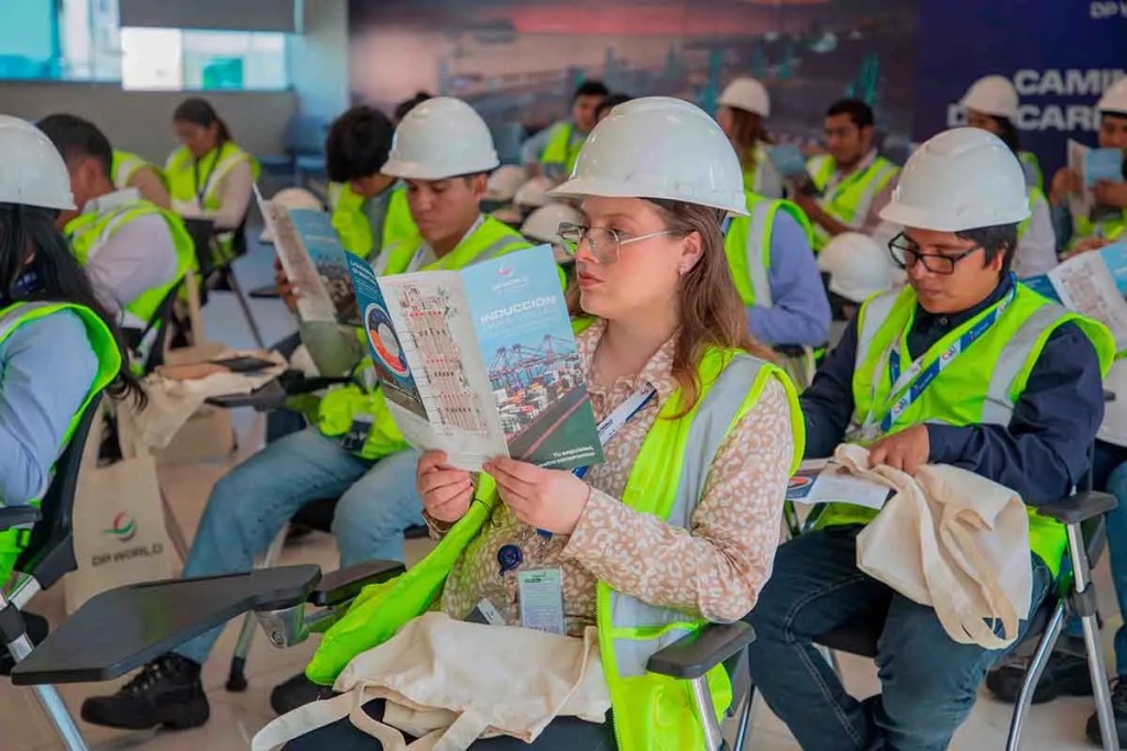 Grupo de estudiantes con cascos y chalecos reflectantes en un evento de inducción, leyendo folletos informativos.