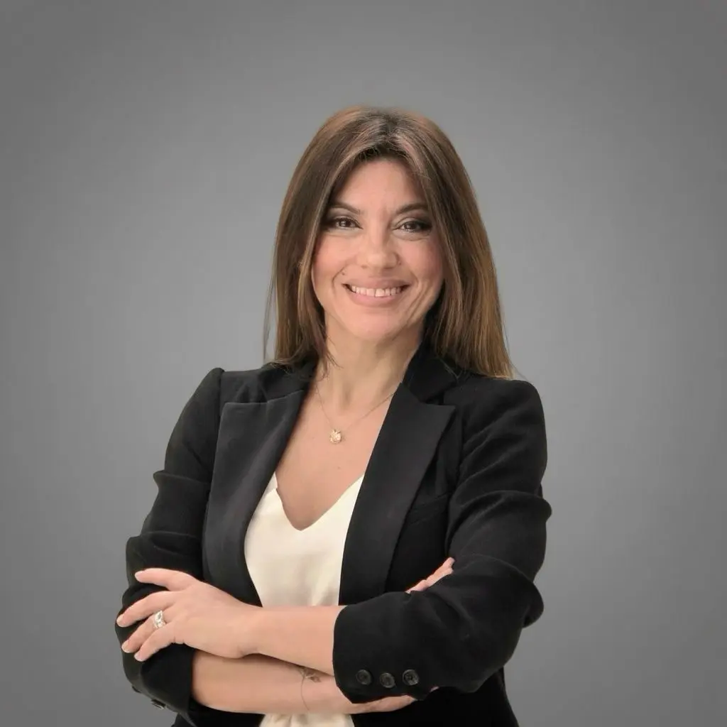 Retrato de Natalia Márquez, nueva gerente general de Visa para Perú, sonriendo y con los brazos cruzados, vestida con un blazer negro sobre una blusa blanca, contra un fondo gris.