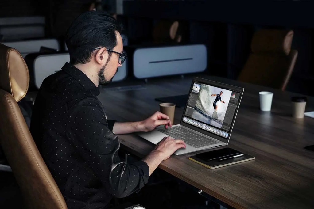 Hombre trabajando en una laptop en un entorno de oficina moderna, editando una imagen de un surfista.