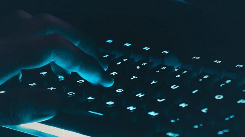 Mano sobre un teclado iluminado en un entorno oscuro.