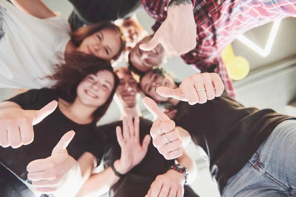 Grupo de personas sonriendo y mostrando los pulgares hacia arriba en un ambiente alegre.