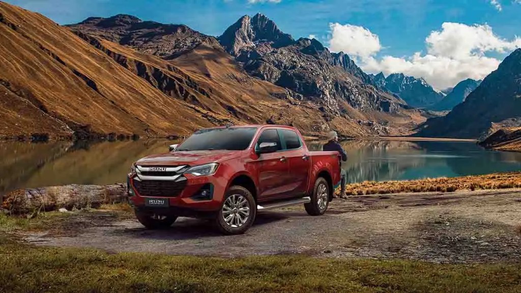 Camioneta Isuzu roja estacionada frente a un lago rodeado de montañas en un paisaje natural.