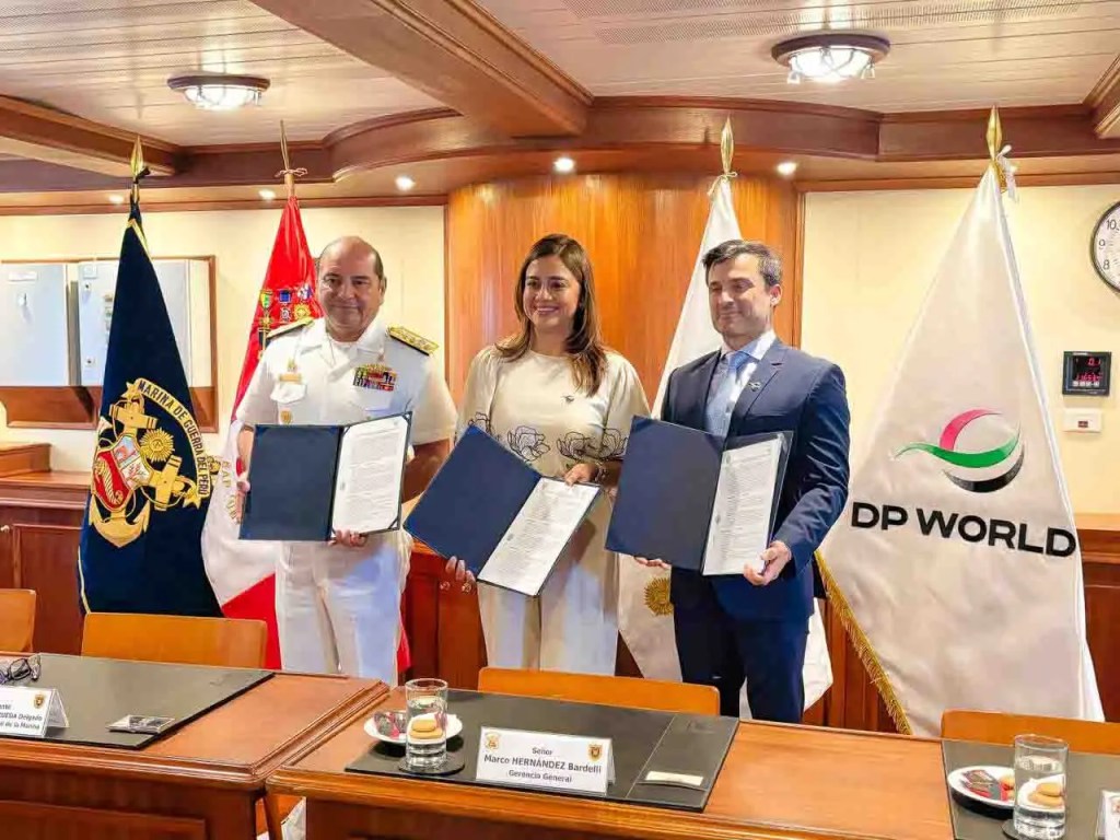 Tres personas sosteniendo documentos en una sala de reuniones, con banderas y símbolos de instituciones marítimas y DP World en el fondo.