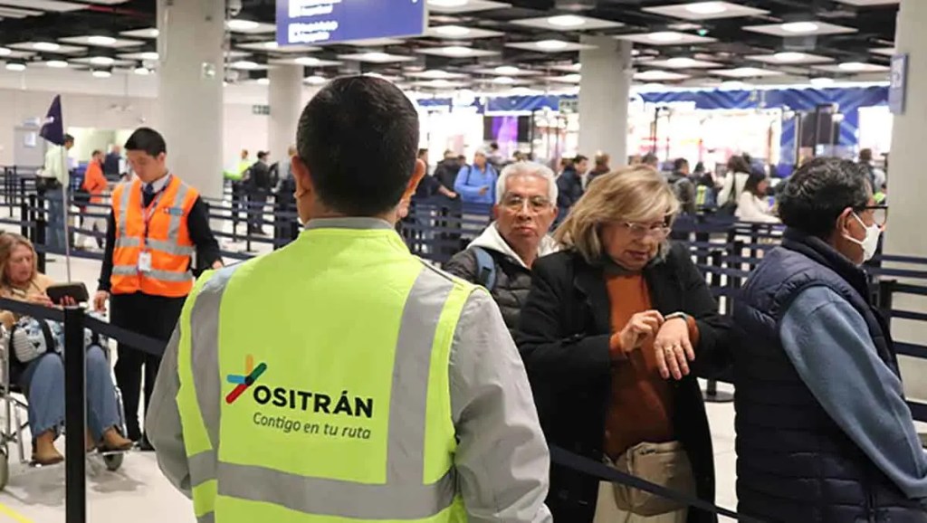 Personal de servicio en un área de espera con pasajeros en una terminal, algunos revisando sus relojes y otros usando dispositivos móviles.