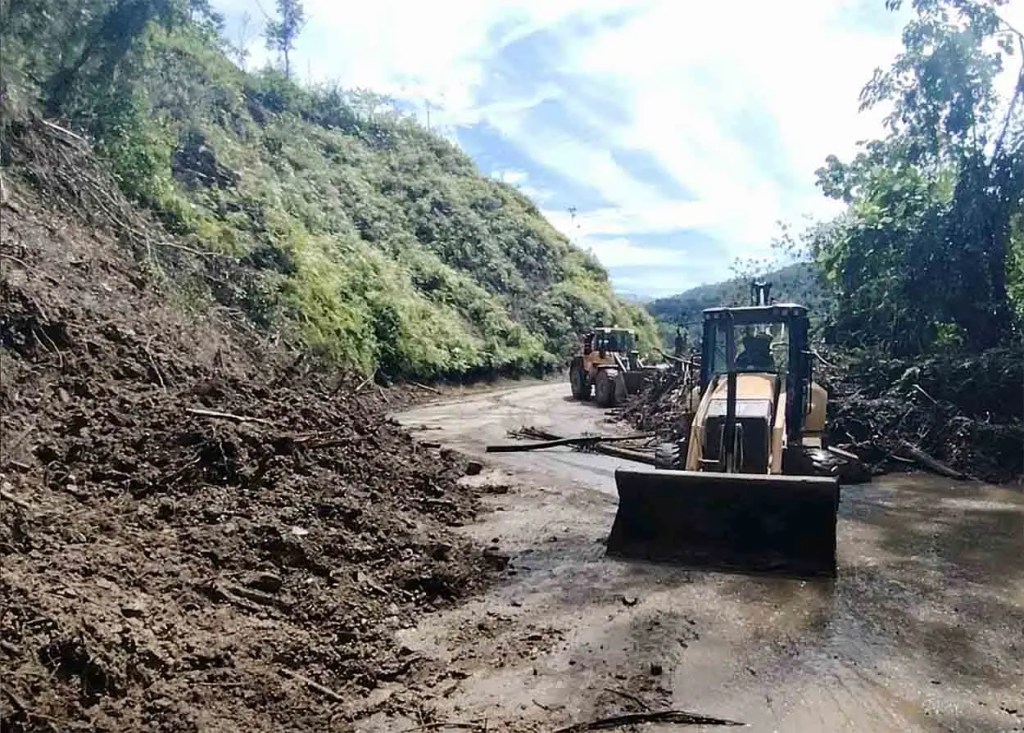 Vista de maquinaria pesada trabajando en una carretera afectada por deslizamientos de tierra en un entorno montañoso.