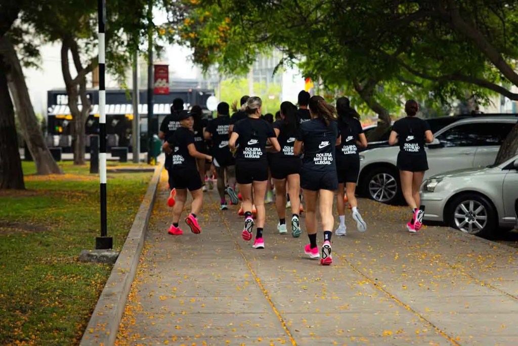 Grupo de mujeres corriendo en un parque, vestidas con camisetas negras de Nike, durante un evento de entrenamiento para la Media Maratón de Lima.