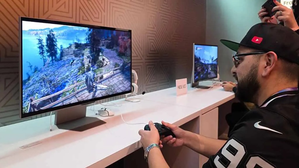 Hombre jugando videojuegos en una consola frente a una pantalla grande que muestra un paisaje virtual.