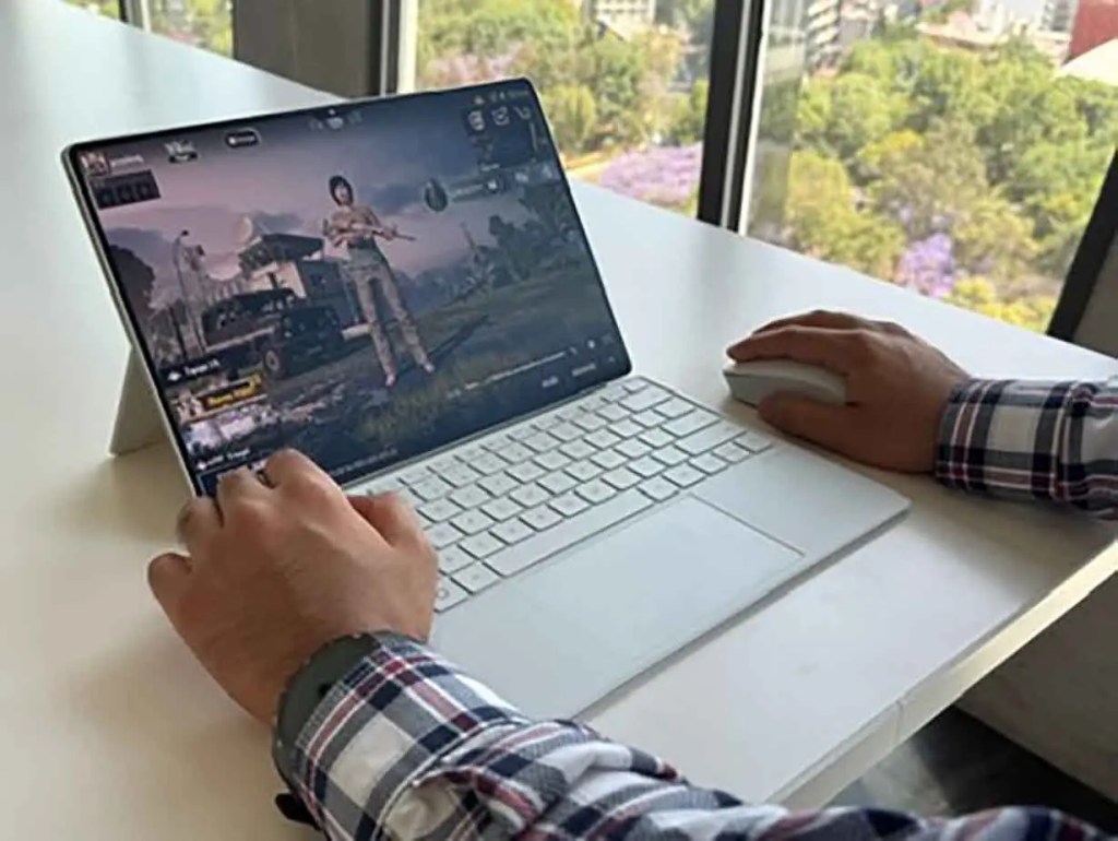 Persona jugando un videojuego en una laptop con teclado y mouse, mostrando una escena del juego en la pantalla.
