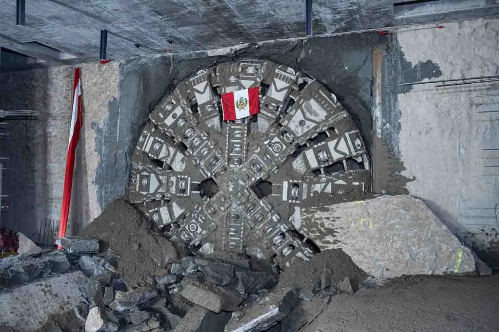 Una tuneladora grande en una construcción, con un fondo de tierra y una bandera de México.