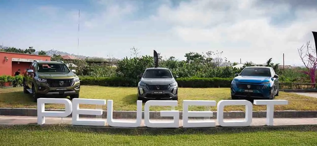 Varios modelos de automóviles Peugeot exhibidos al aire libre, con un letrero grande que dice 'PEUGEOT' en primer plano.