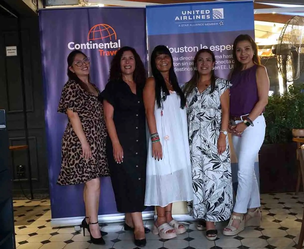 Grupo de cinco mujeres sonrientes en un evento, de pie frente a banners de Continental Travel y United Airlines.