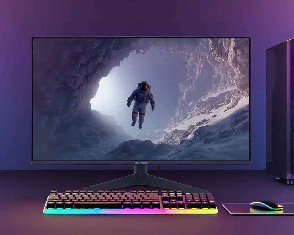 Monitor con una imagen de un astronauta flotando en una cueva, con un teclado RGB y un mouse al lado.