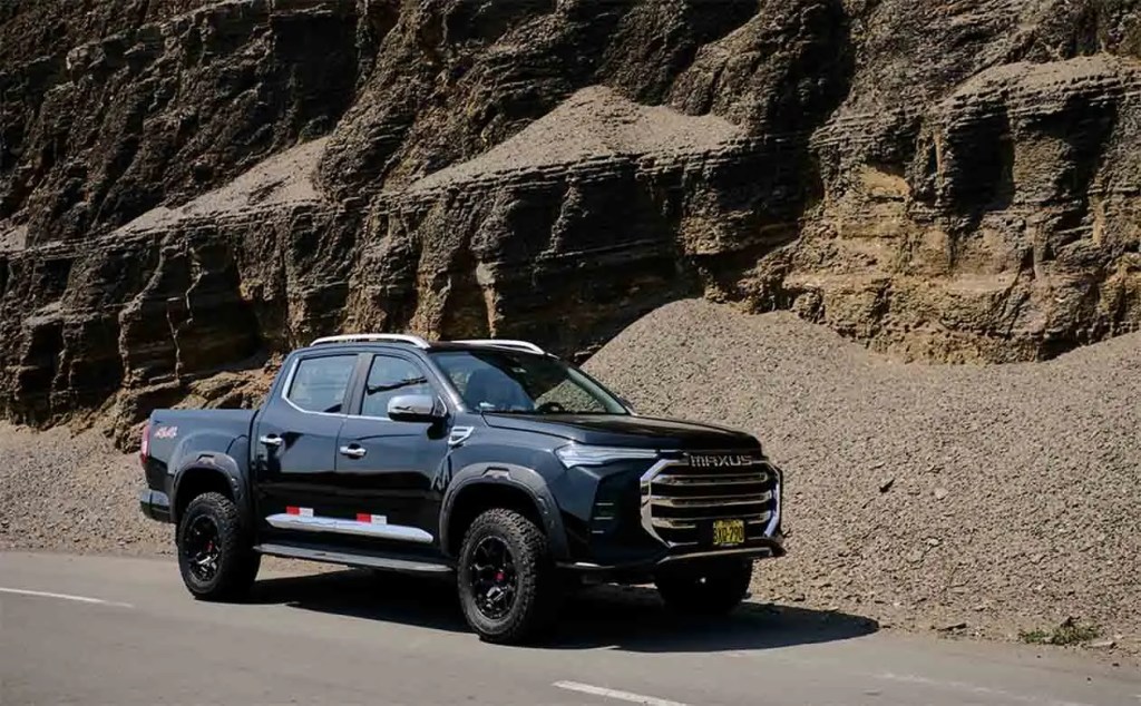 Camioneta negra de perfil estacionada junto a una colina de rocas y grava.