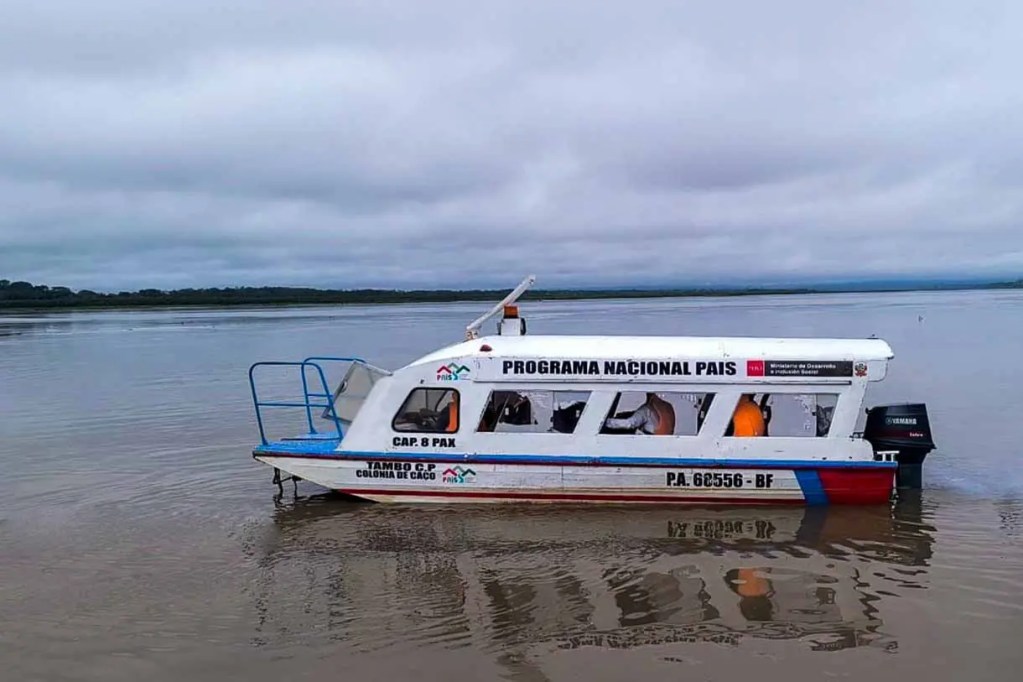 Una embarcación blanca y azul con el texto 'PROGRAMA NACIONAL PAÍS' navega en un río bajo un cielo nublado.