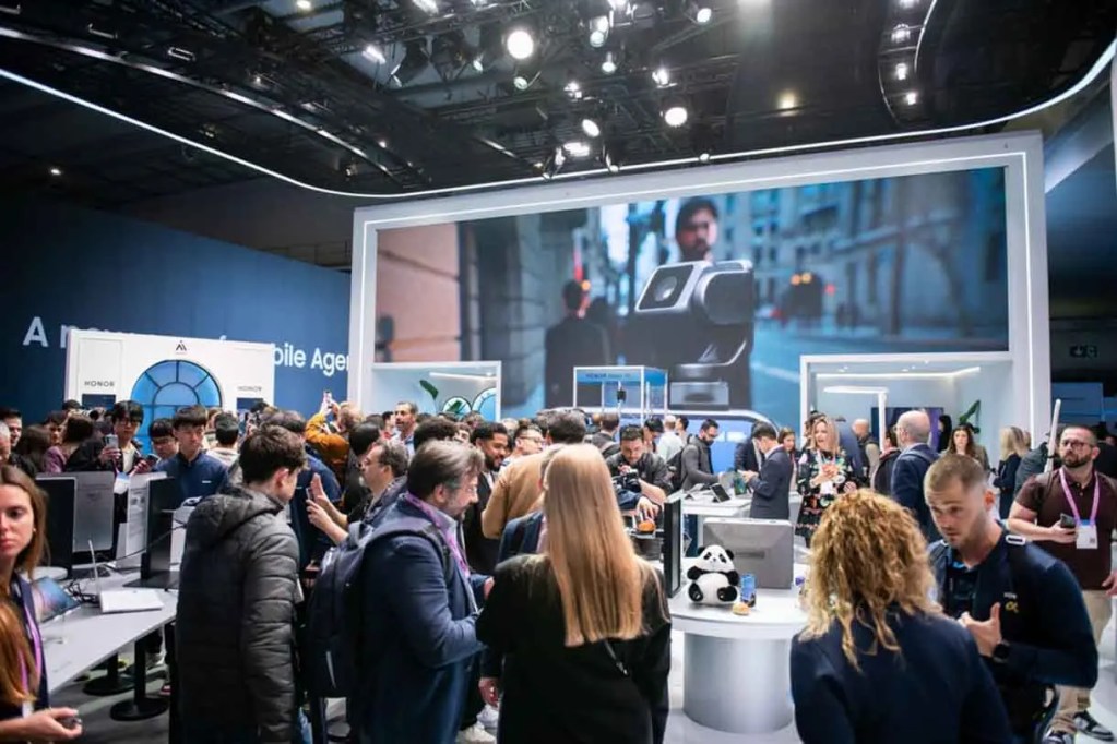 Multitud de personas en un evento tecnológico, interactuando en un stand con pantallas y dispositivos electrónicos.