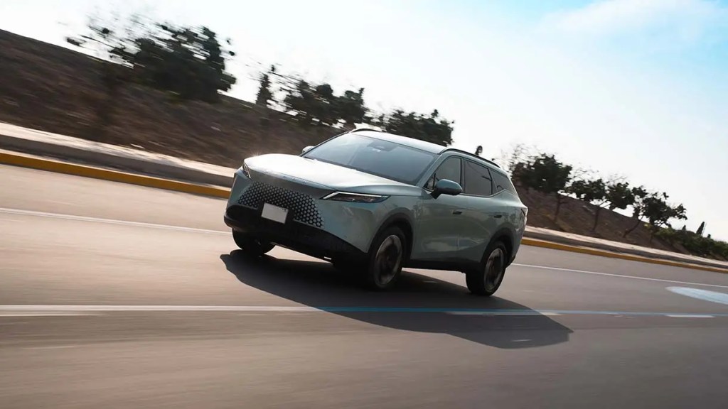 Vehículo SUV moderno en movimiento sobre una carretera con un paisaje arbolado al fondo.