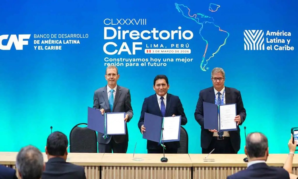 Tres hombres con trajes formales sosteniendo documentos en una conferencia de prensa, bajo un fondo que muestra el logo del CAF y el mapa de América Latina y el Caribe.
