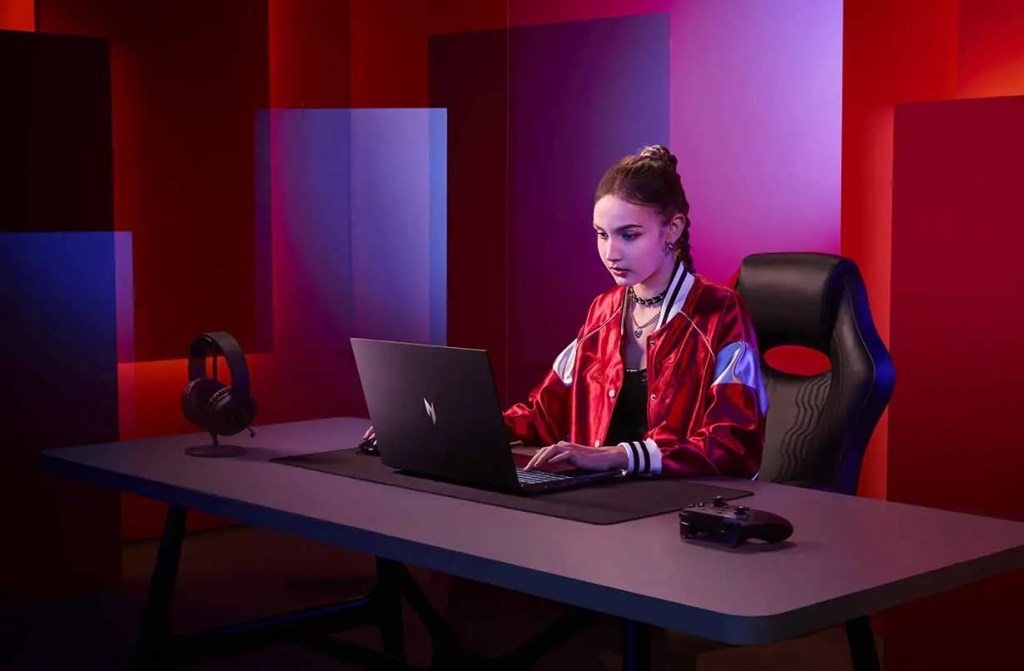 Joven jugando en una computadora portátil en un ambiente con luces rojas y azules, usando auriculares y con un control al lado.