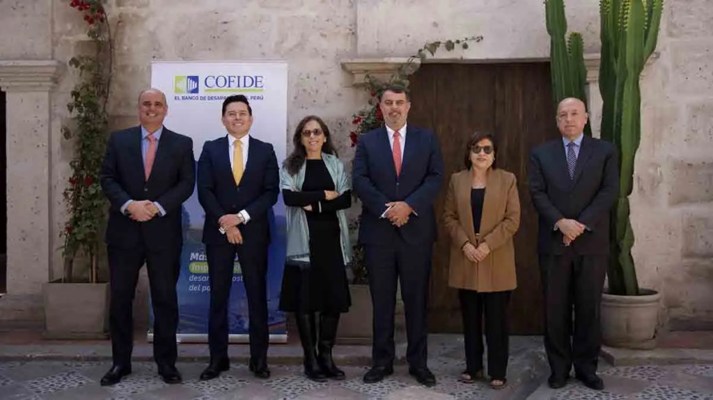 Grupo de seis personas posando para una foto frente a un mural con el logotipo de COFIDE en un ambiente exterior.