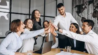 Grupo de personas en una reunión de negocios, levantando las manos en señal de celebración y colaboración.