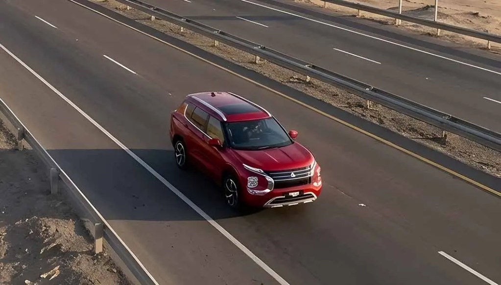 Un coche rojo circulando por una carretera amplia con línea divisoria.