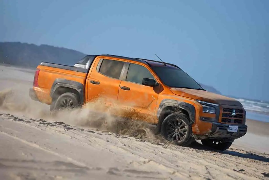 Camioneta naranja conduciendo sobre la playa, levantando arena.