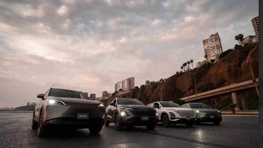 Cuatro SUVs modernas en una carretera, con un paisaje urbano y un cielo nublado al fondo.