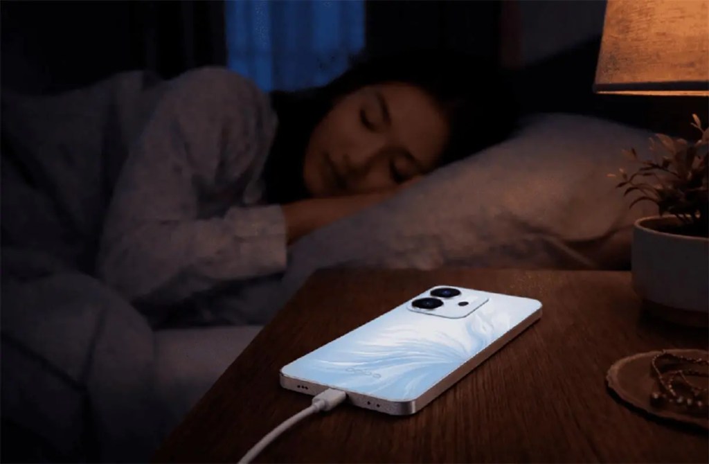 Una mujer dormida en la cama junto a una mesita de noche con un teléfono móvil blanco cargándose.