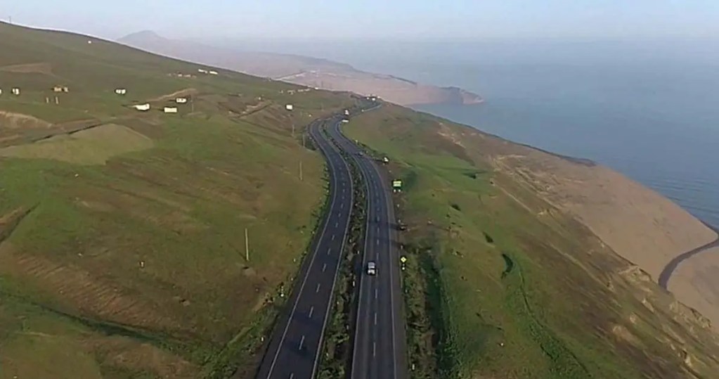 Vista aérea de una carretera que serpentea a lo largo de un acantilado verde, con el océano en el fondo.