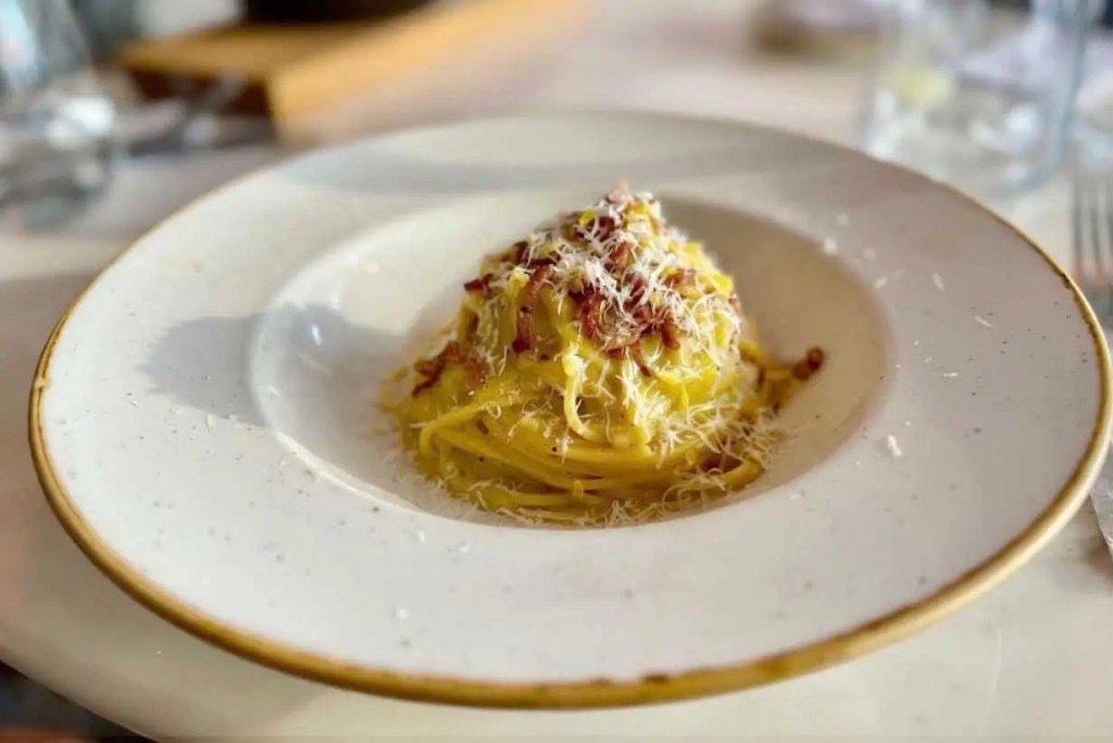 Plato de pasta con salsa cremosa, trozos de tocino y queso rallado sobre un fondo de mesa.