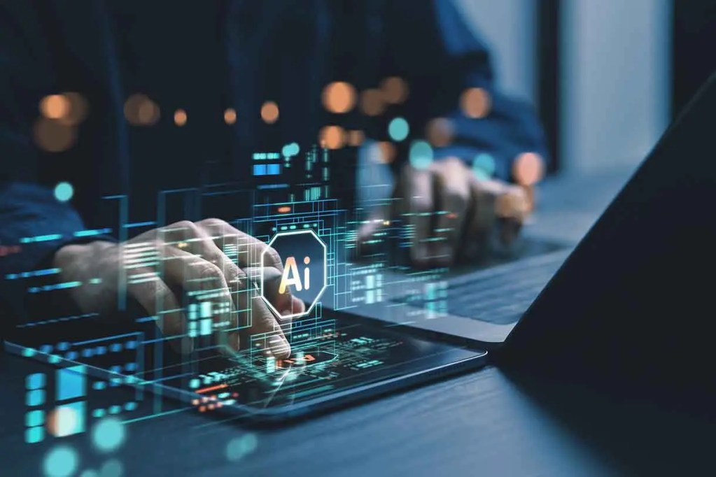 Manos utilizando una tableta y un ordenador portátil, con gráficos digitales y el símbolo 'AI' sobreimpreso, representando la inteligencia artificial.