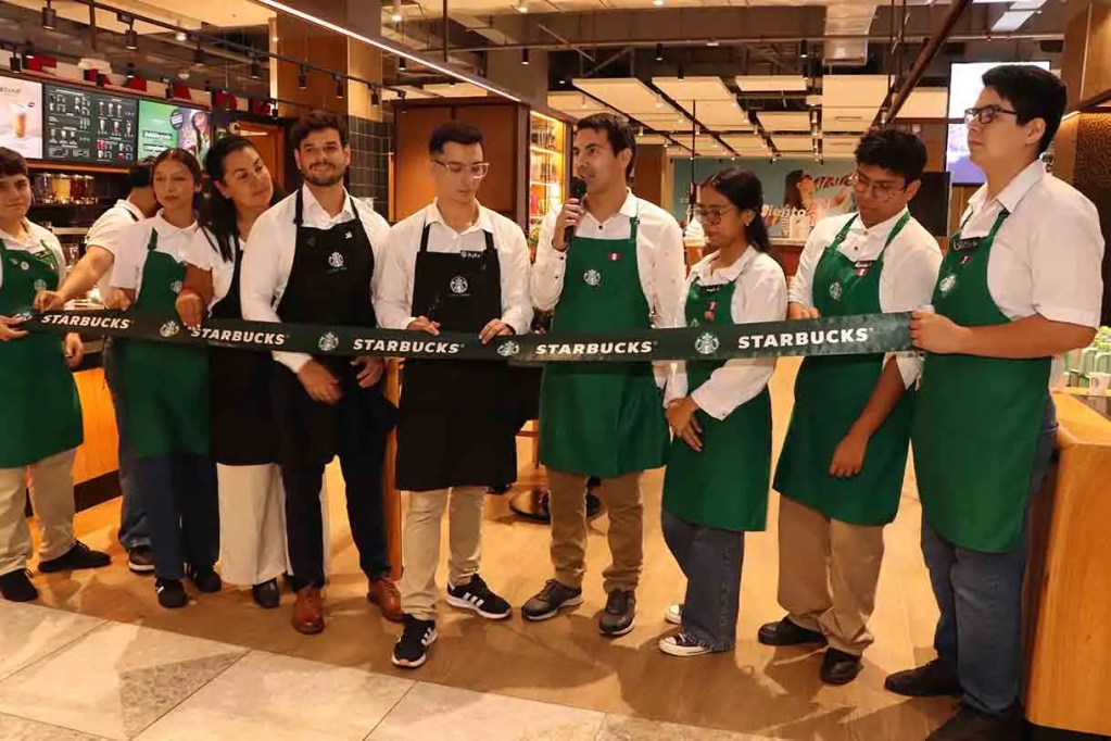 Grupo de empleados de Starbucks en una ceremonia de inauguración, sosteniendo una cinta con el logo de la marca.